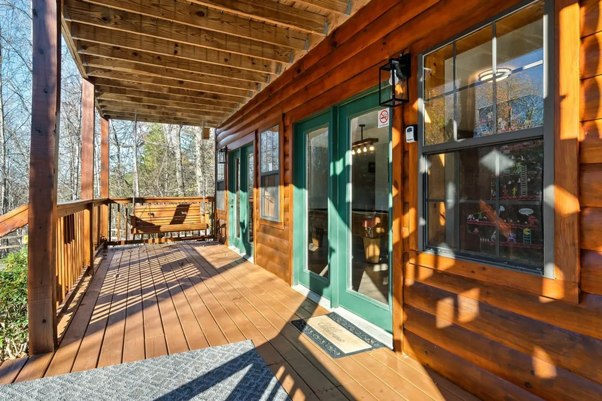 An inviting wooden deck set against lush natural surroundings, featuring green doors, a hanging swing, and open space ideal for small groups to gather. The deck is immersed in the outdoors, providing a seamless transition from indoor activities to fresh air and scenic views, perfect for laughter and camaraderie after a day out.