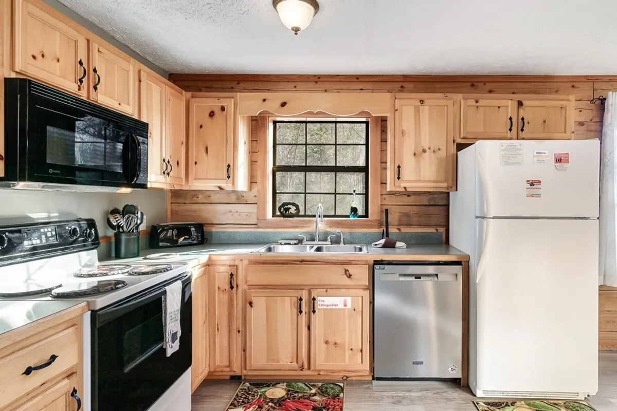 A cozy, inviting kitchen with warm wooden cabinetry, modern appliances, and a window providing a view to the outdoors. The kitchen sink and counters are ready for meal prep, while personal touches create a homey atmosphere. The setup suggests an ideal spot for collaborative cooking and morning rituals alike.