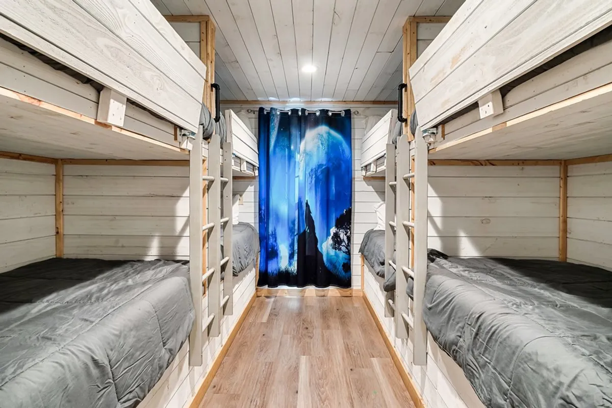 This image captures a playful bunk room featuring multiple bunk beds partially concealed by a decorative curtain. The setup suggests a cozy, fun, and communal sleeping arrangement ideal for kids or groups. The atmosphere is whimsical and inviting, perfect for imaginative play or late-night storytelling.
