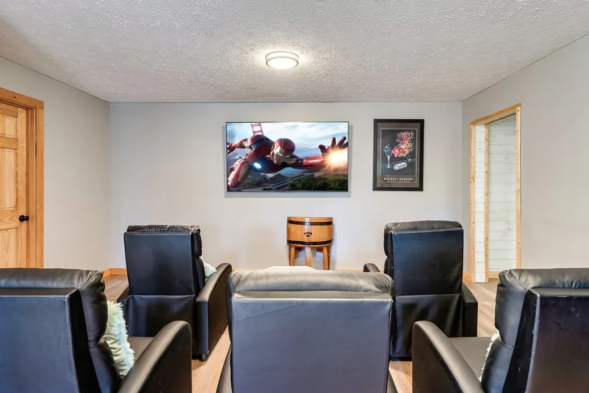 A cozy media area is depicted, complete with leather recliner chairs facing a large TV (showing a superhero image) and surrounded by themed wall art and a unique barrel table, ideal for movie nights and video gaming marathons.