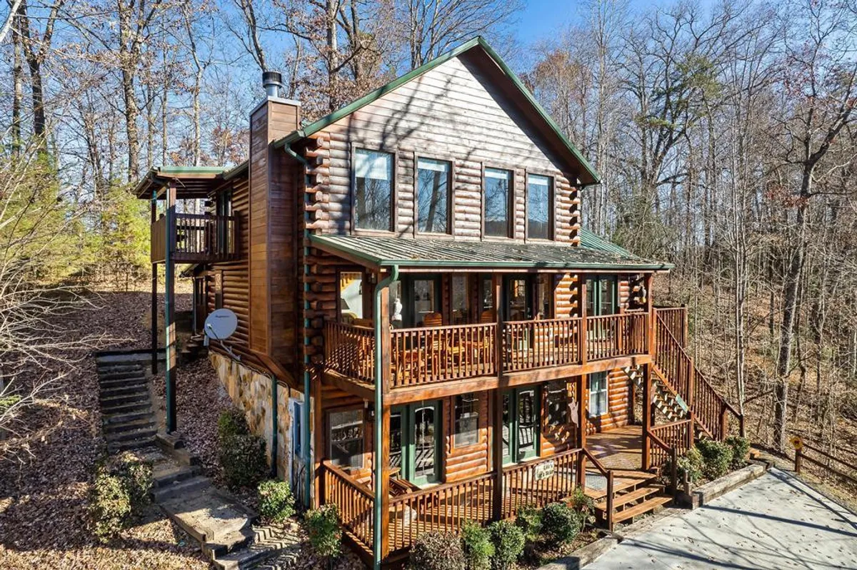 A classic log cabin with multiple balconies rises amidst a backdrop of lush trees. The wide staircase and expansive decks suggest ample space for family gatherings and outdoor relaxation after a day of adventures. The serene setting invites guests to unwind while remaining connected to the surrounding wilderness.