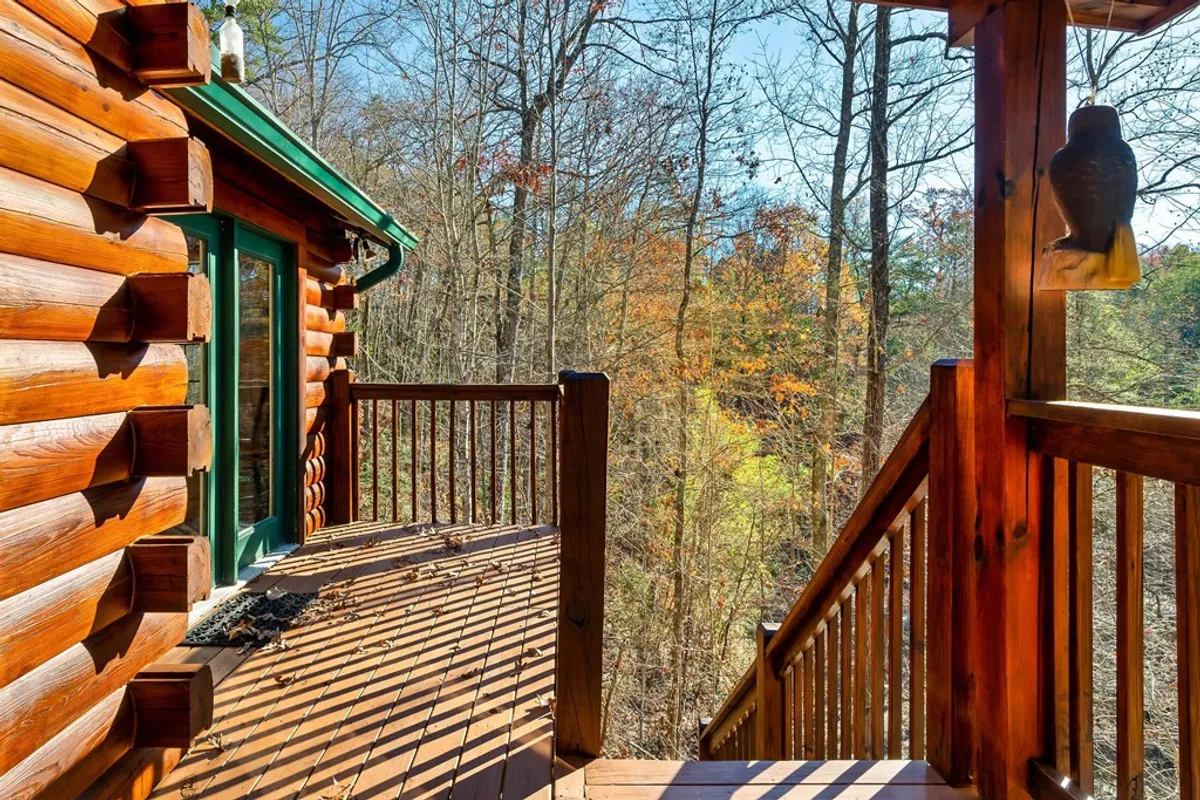 A peaceful deck view featuring a rustic log cabin structure, wooden railings, and a sweeping forest vista. The setting is tranquil and suggests easy access to nature, while also hinting at spaces for outdoor relaxation and gatherings.