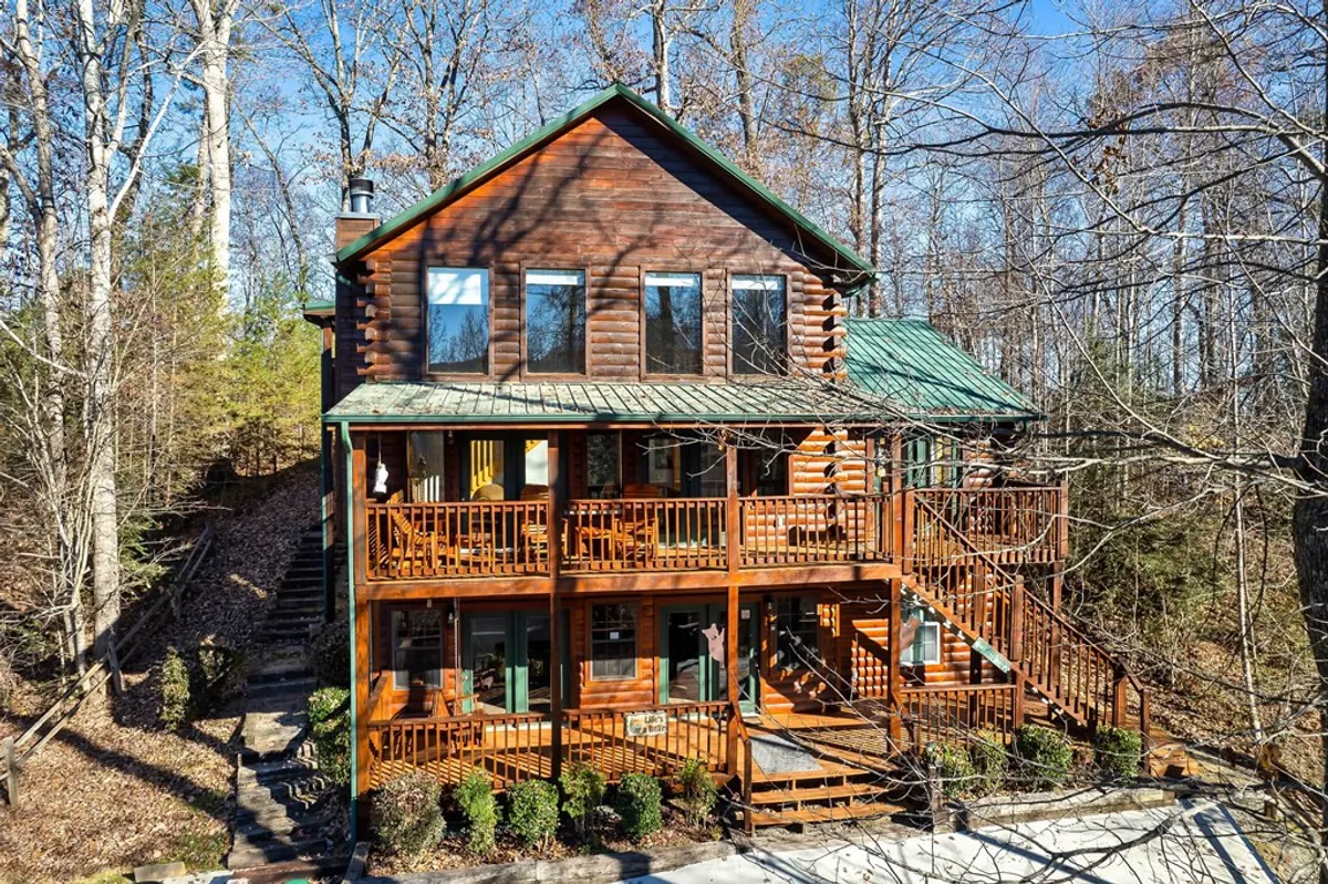 A welcoming log cabin is framed by greenery and features multiple decks, perfect for enjoying mornings with coffee or evenings under the stars. The inviting exterior hints at memorable family moments on the deck, sharing stories after days spent at top attractions or on nearby trails.