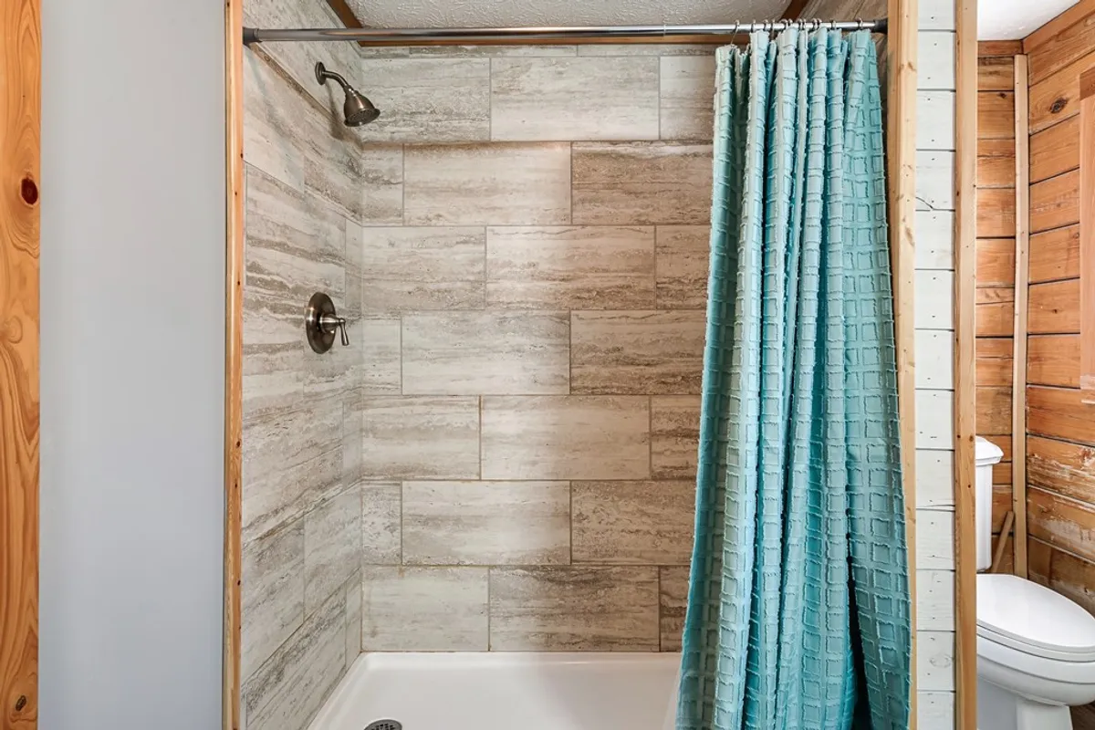 A modern bathroom featuring a spacious shower with a blue curtain and textured wall tiles. The space is clean and calming, designed for refreshing showers and moments of relaxation.