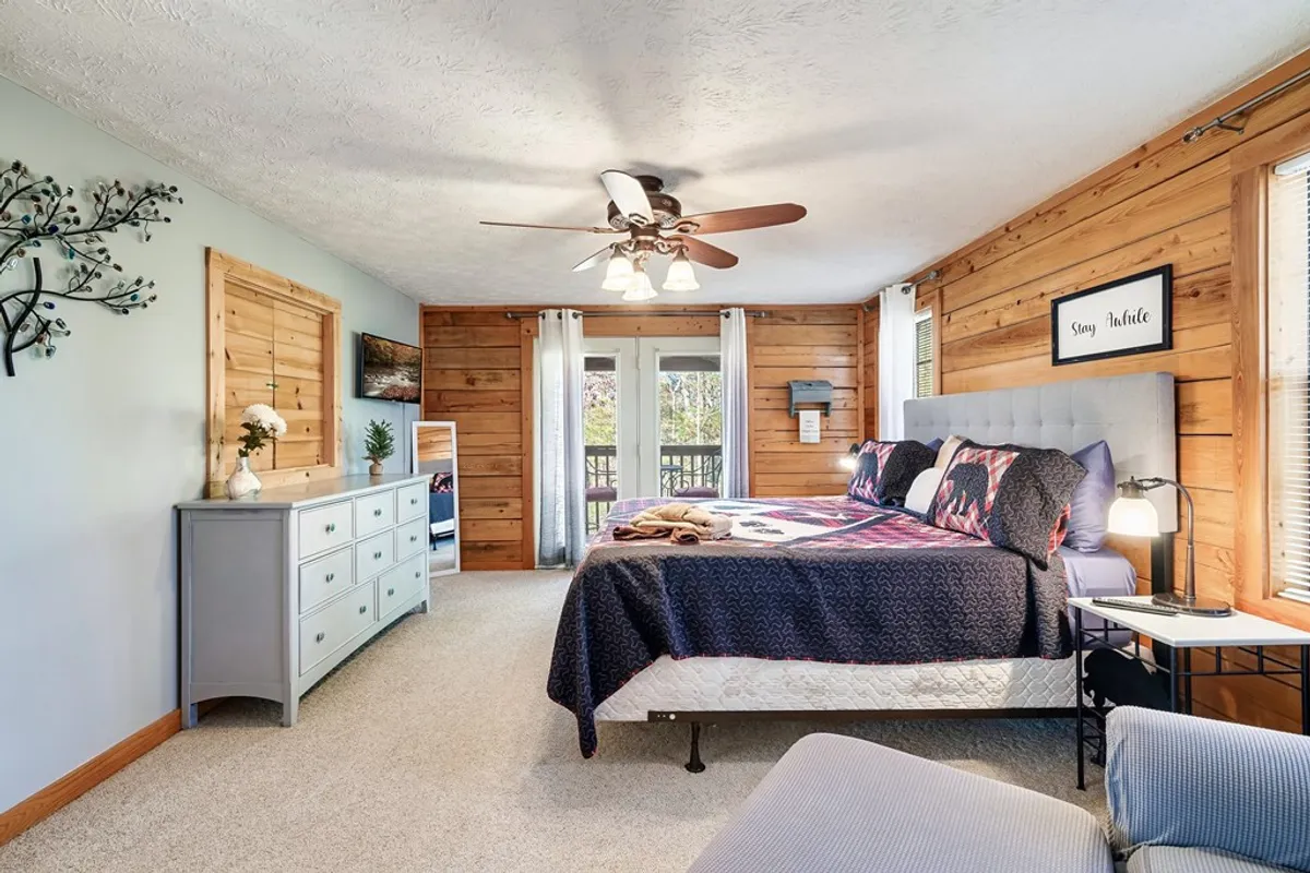 A tranquil bedroom with a cozy bed, a dresser, sliding doors, and decorative wall art. Natural light pours in through the glass, creating a bright, airy feel. The space is uncluttered and comfortable, ideal for unwinding.