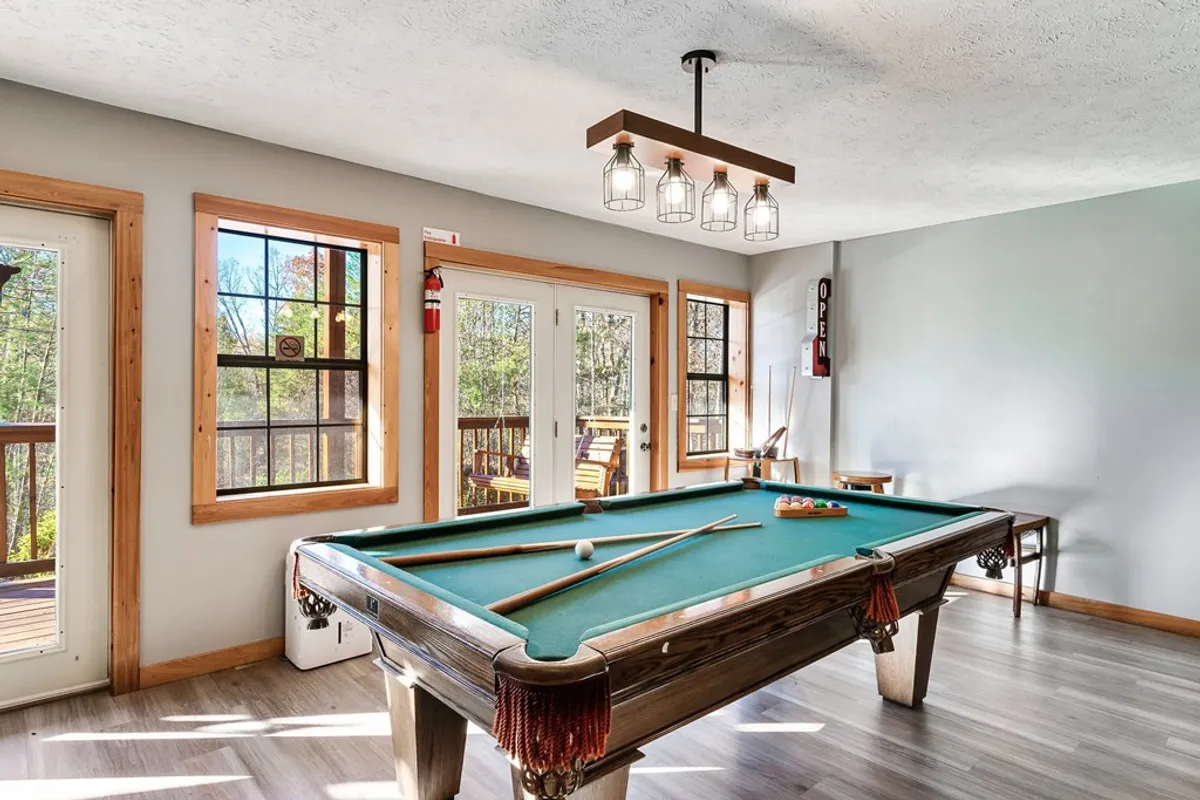 This image showcases a stylish pool table set in a bright room with large windows and modern lighting. The space is designed for group play, with ample room around the table for movement and socializing, capturing the playful and inviting nature of the game room.
