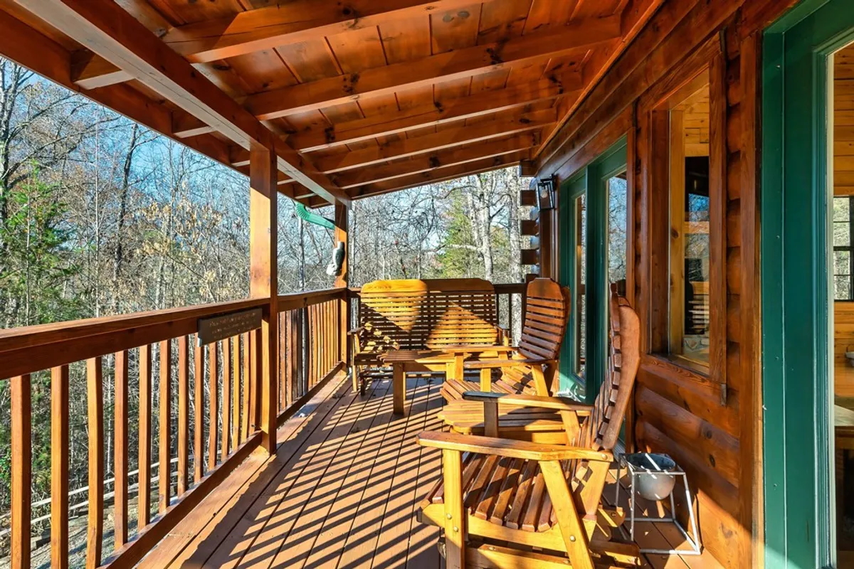 A cozy porch scene with wooden rocking chairs facing out toward surrounding trees, framed by a rustic wooden railing. The tranquil atmosphere and inviting seating emphasize relaxation and appreciation of the natural surroundings.